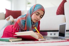 AN women student wearing a hijab studies at home, using a notebook, pen and laptop